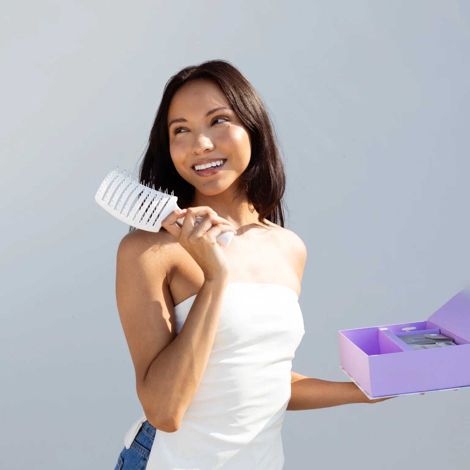 Woman smiling, holding a hairbrush and a purple gift box.