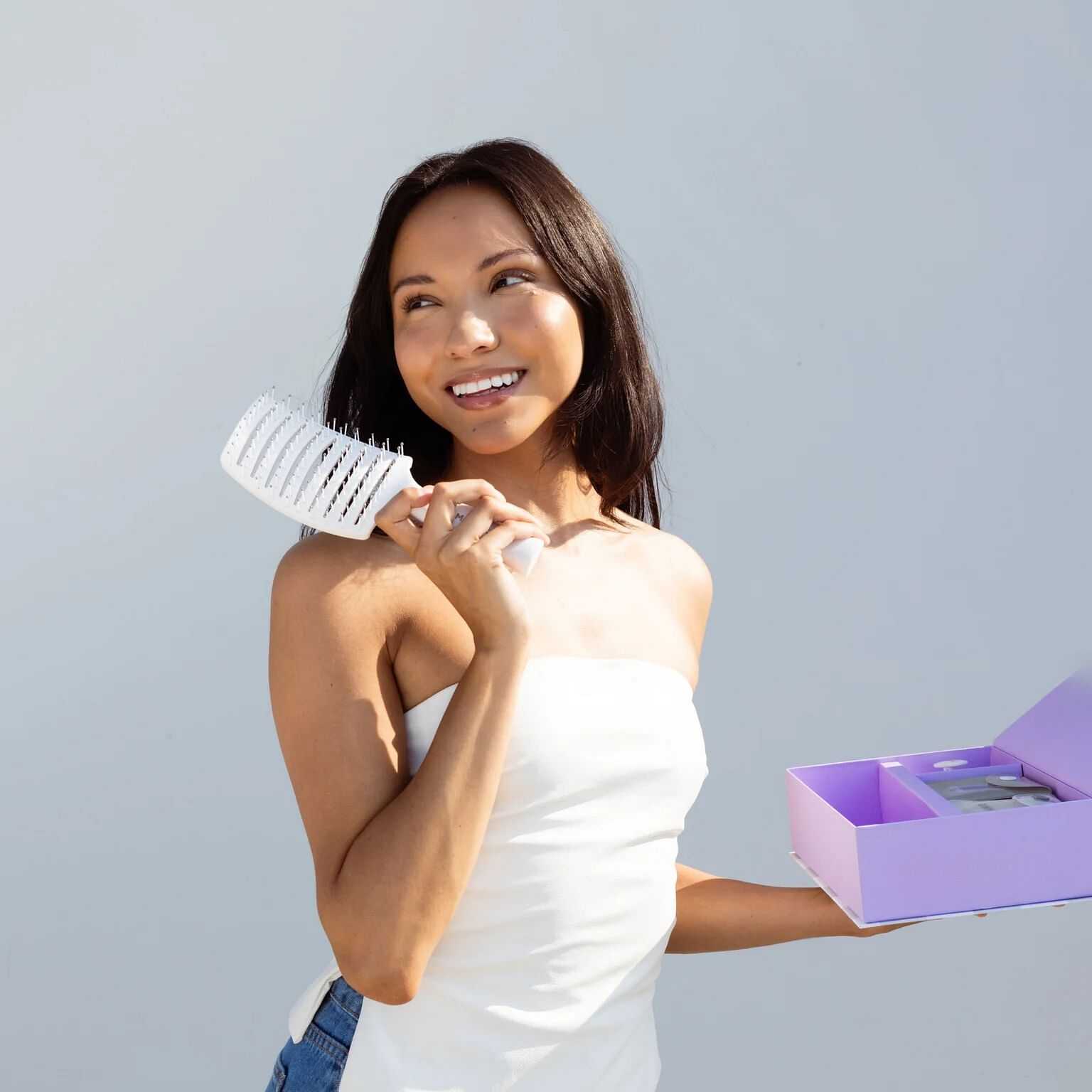 Woman smiling, holding a hairbrush and a purple gift box.
