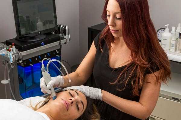 Aesthetician performing a facial treatment on a woman lying down in a skincare clinic.