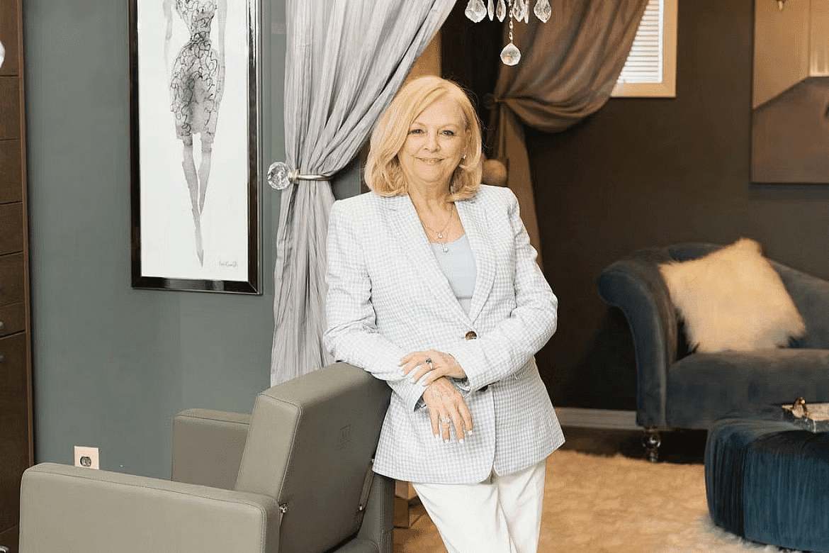 Woman in a stylish salon, standing by a modern hairdresser's chair with a chandelier above.