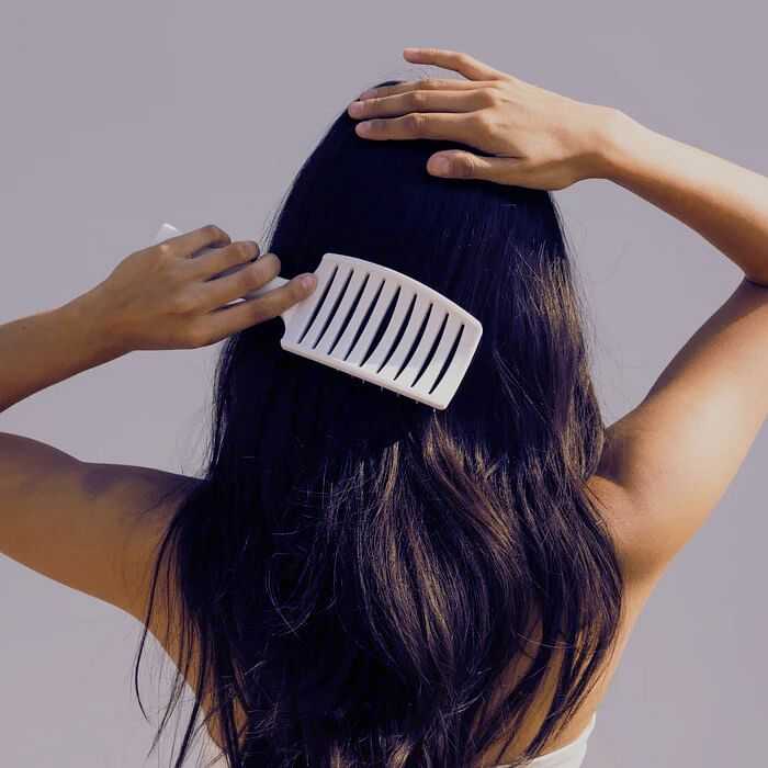 Person brushing long, dark hair with a wide-toothed comb against a plain background.